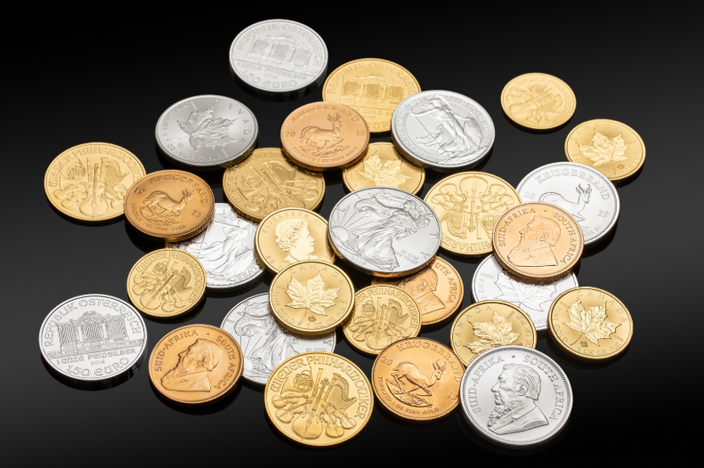 Various gold and silver bullion coins from global mints, including Eagles, Maple Leafs, Philharmonics, and Krugerrands, arranged on a black surface.